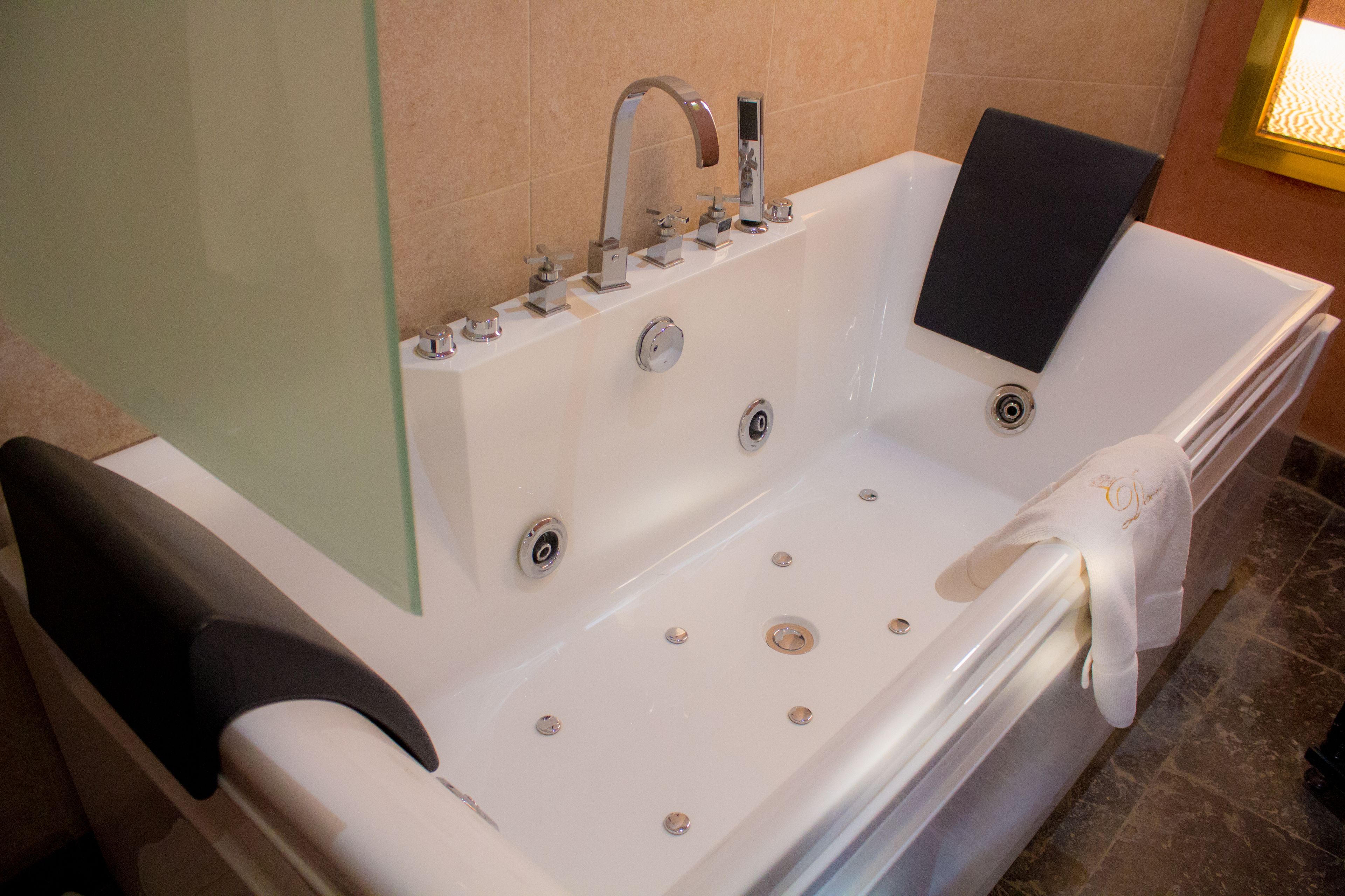 A modern bathroom with a large bathtub, a glass shower enclosure, and a black towel on the edge.