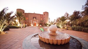 Un patio con una fuente, palmeras y un edificio con una torre redonda.