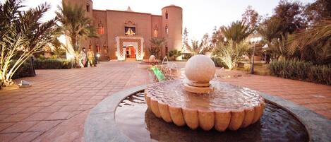 A courtyard with a fountain, palm trees, and a building with a round tower.