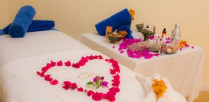 A spa room with two beds, blue towels, a heart-shaped flower arrangement, and various spa products on a table. - Palais du Desert Hôtel & Spa (Aarab Sebbah Ziz)