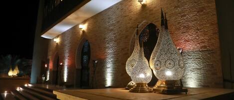A building facade with a textured brick wall, illuminated by wall-mounted lights and decorative lamps.