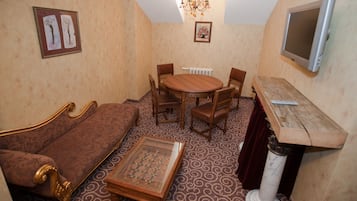 Ein gemütliches Zimmer mit einem runden Holztisch, vier Stühlen, einem Sofa, einem kleinen Holztisch und einem an der Wand montierten Fernseher.