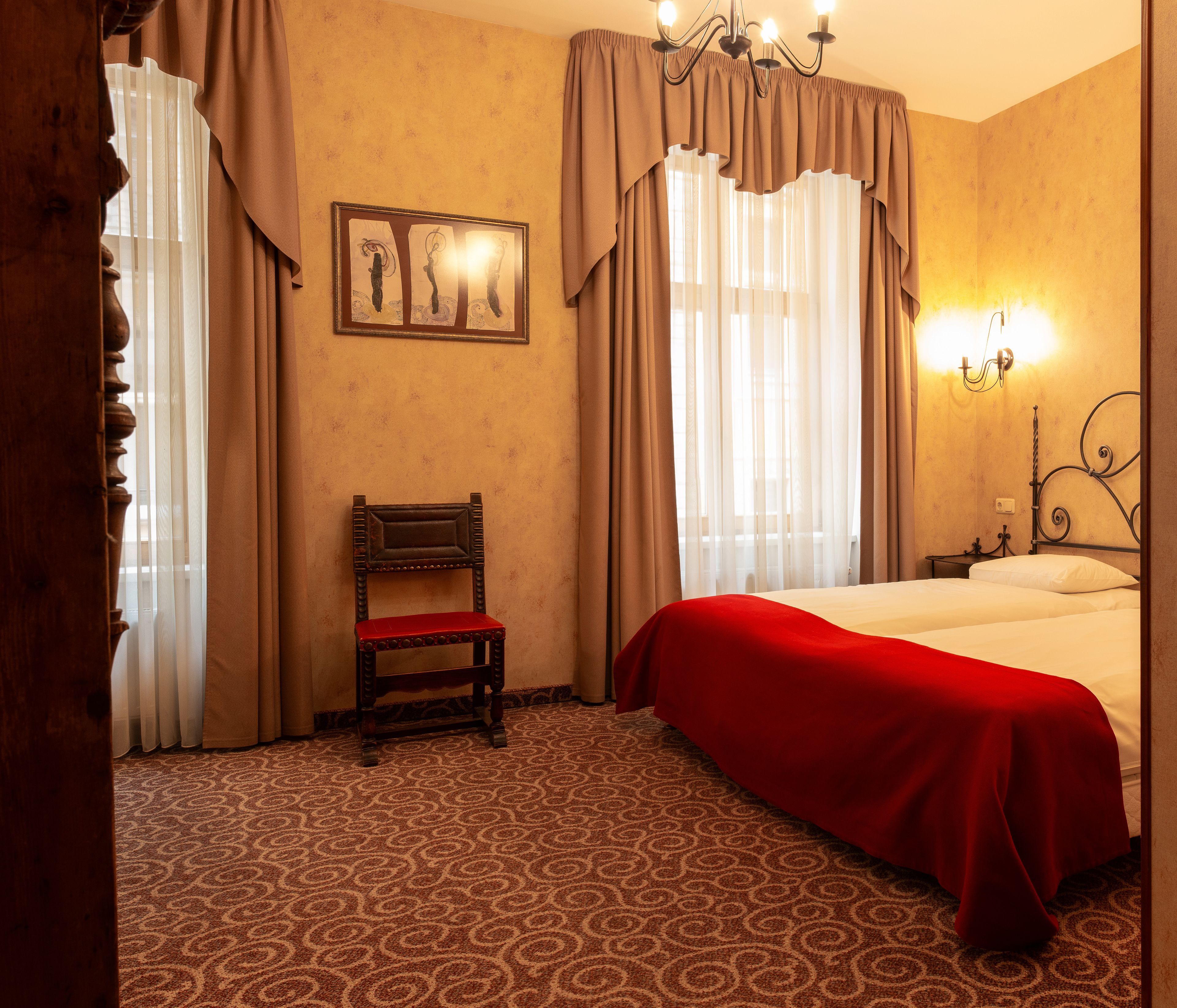 Habitació d'hotel amb un llit, una cadira, una làmpada de cristall i un quadre a la paret.