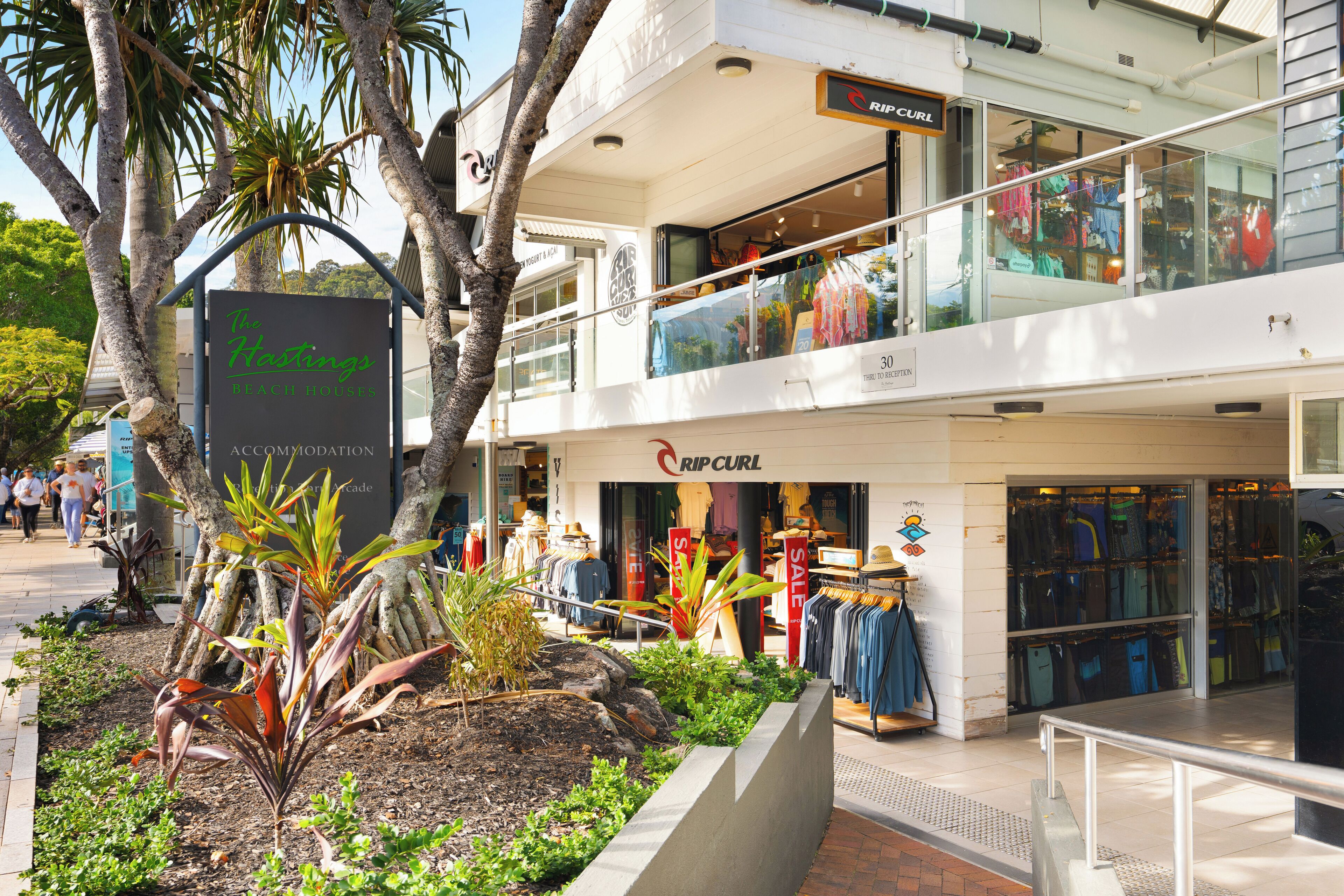 A modern shopping mall with a clothing store named 'Rip Curl' and a sign for 'The Kestings Beach House' accommodation.