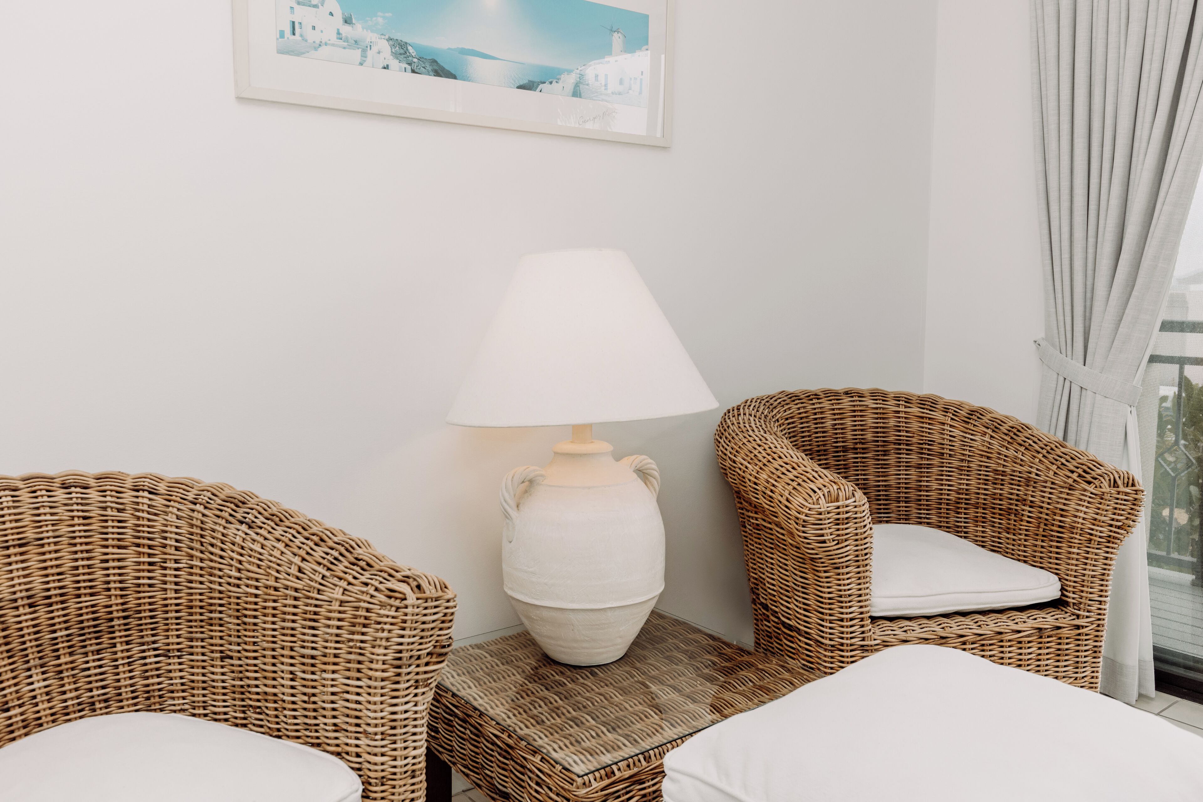 A room with wicker furniture, a white lamp, and a framed picture on the wall.