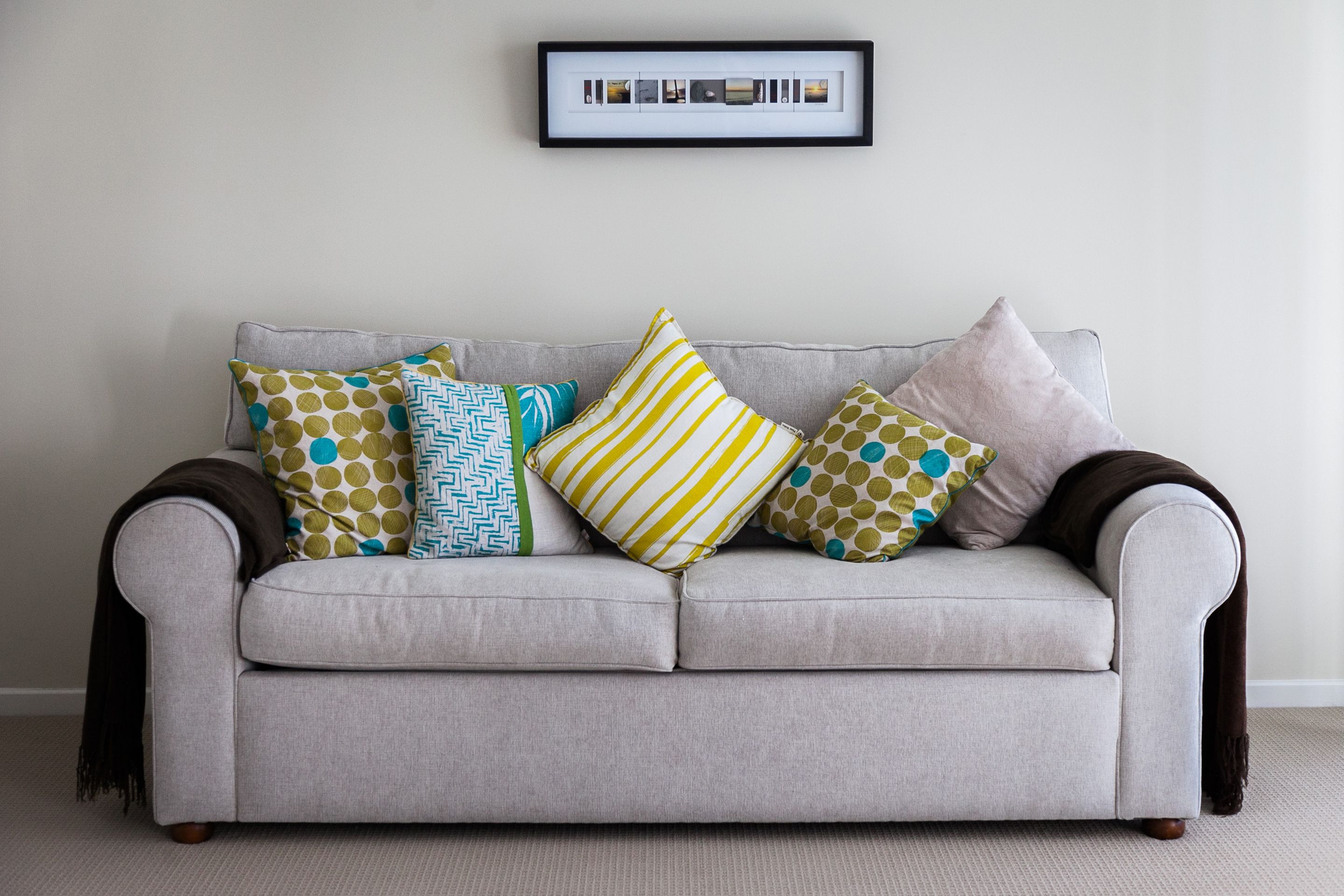 A grey sofa with multiple patterned cushions against a plain wall, with a framed photo above.
