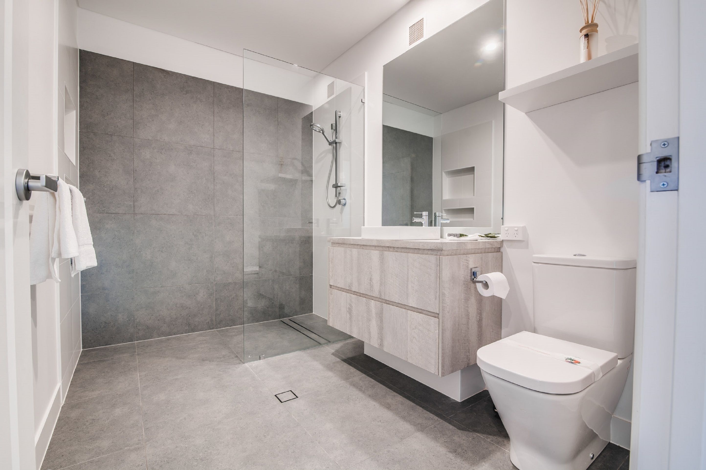 A modern bathroom with a glass-enclosed shower, a wooden vanity, and a white toilet.