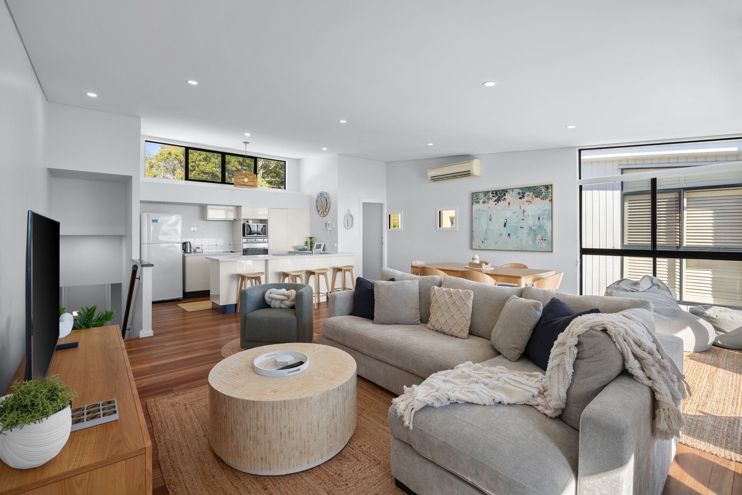 A modern living room with a sofa, coffee table, and a dining area with a kitchen in the background.