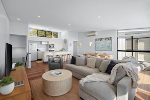 A modern living room with a sofa, coffee table, and a dining area with a kitchen in the background.