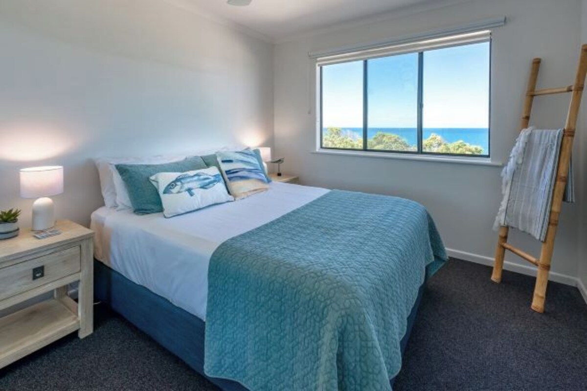 Un dormitorio con cama, mesita de noche, lámpara, ventana con vistas y escalera de madera.