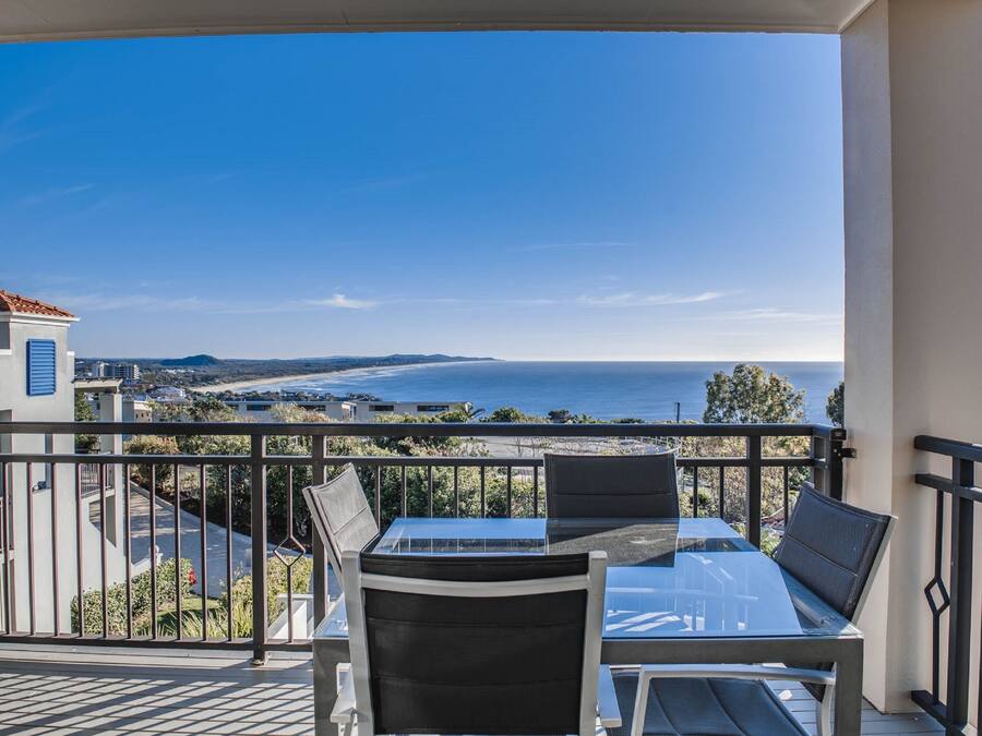 A balcony with a table and chairs overlooking a beach and ocean.