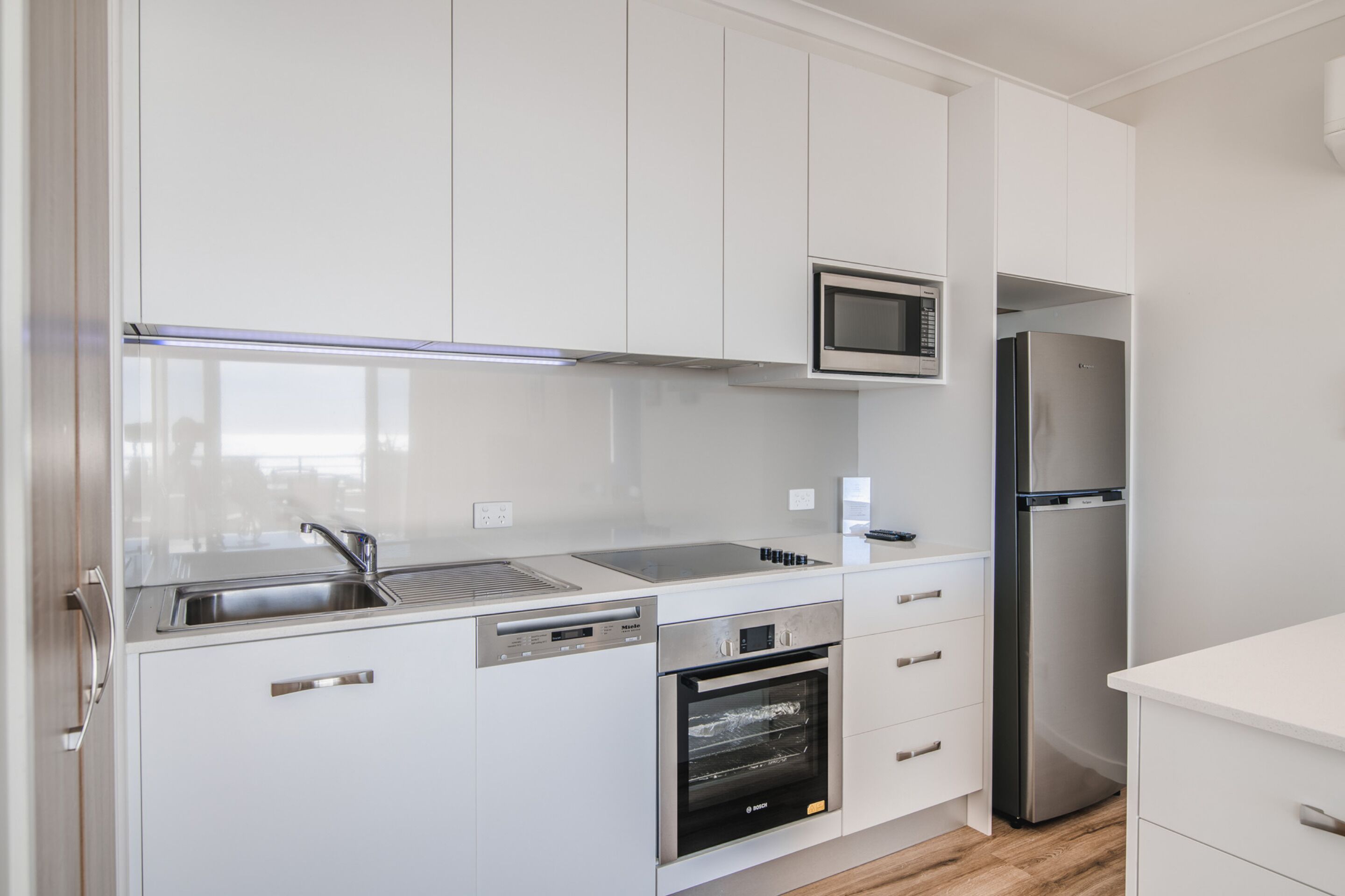 A modern kitchen with white cabinets, a stainless steel refrigerator, a microwave, and an oven.