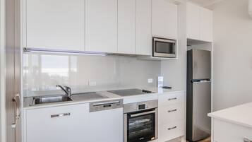 A modern kitchen with white cabinets, a stainless steel refrigerator, a microwave, and an oven.