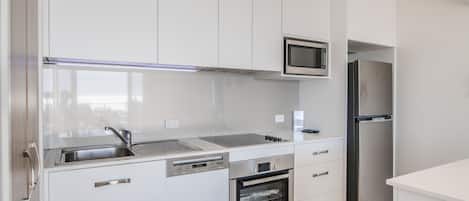 Una cocina moderna con armarios blancos, un refrigerador de acero inoxidable, un microondas y un horno.