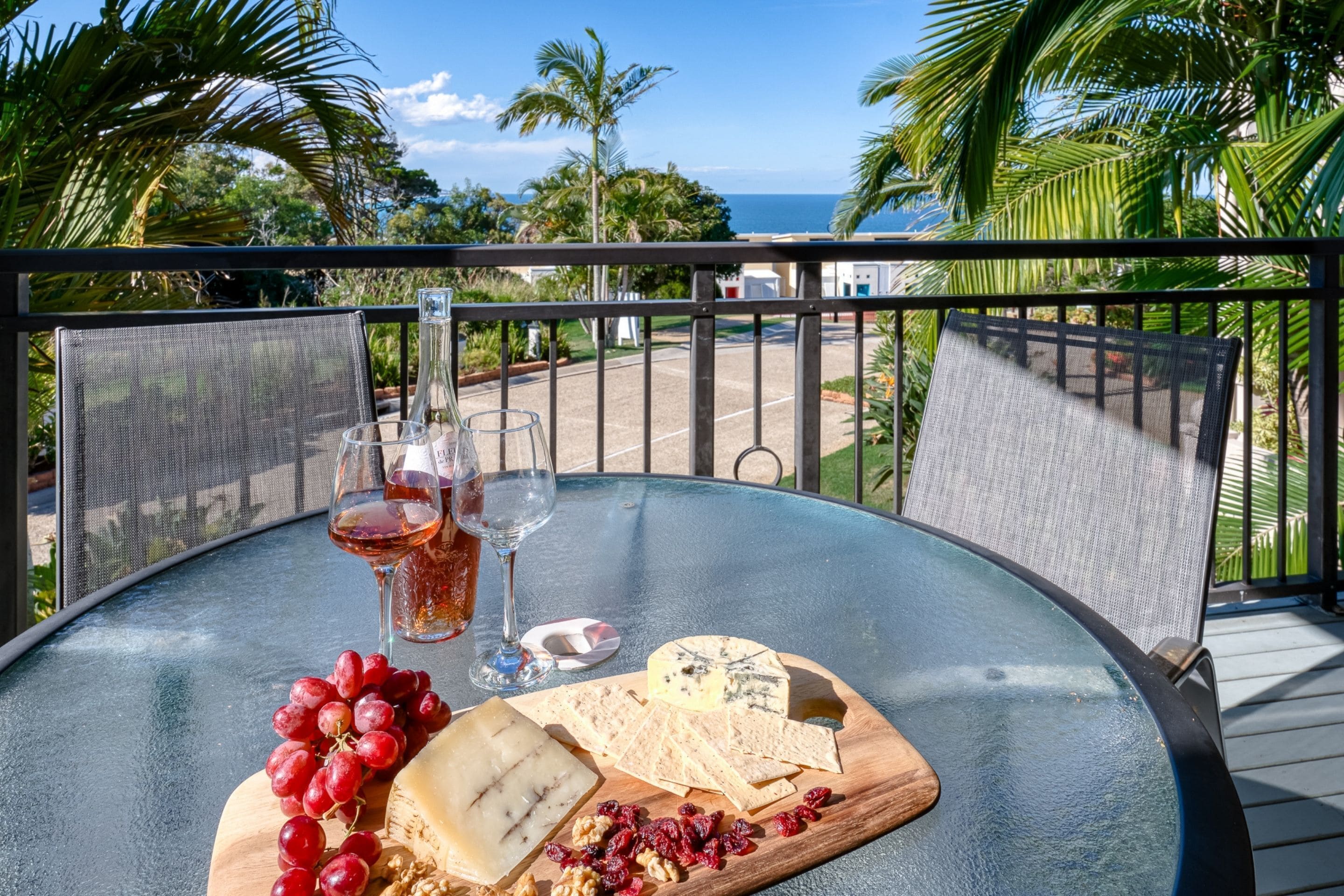 Ein Tisch mit Käseplatte, Trauben und Weingläsern auf einem Balkon mit Blick aufs Meer.