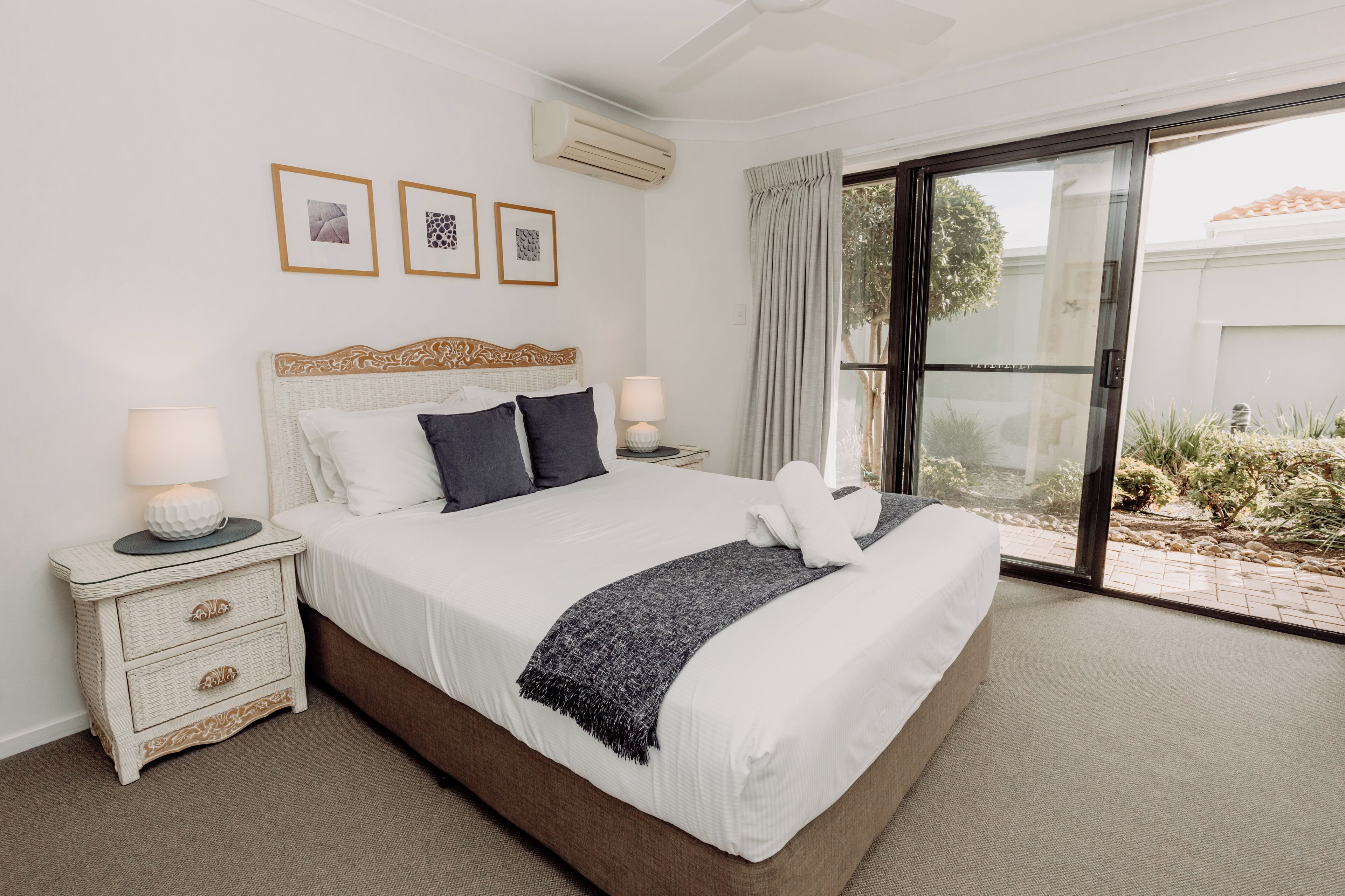 A bedroom with a large bed, two bedside tables with lamps, a window with curtains, and framed pictures on the wall.