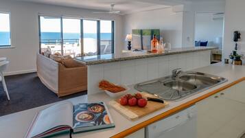 Une cuisine moderne dotée d’un grand îlot central, d’un coin repas offrant une vue sur l’océan et d’un espace salon confortable.