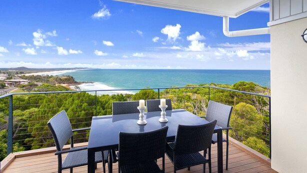 Ein Balkon mit Tisch und Stühlen, der Blick auf die Küste freigibt.