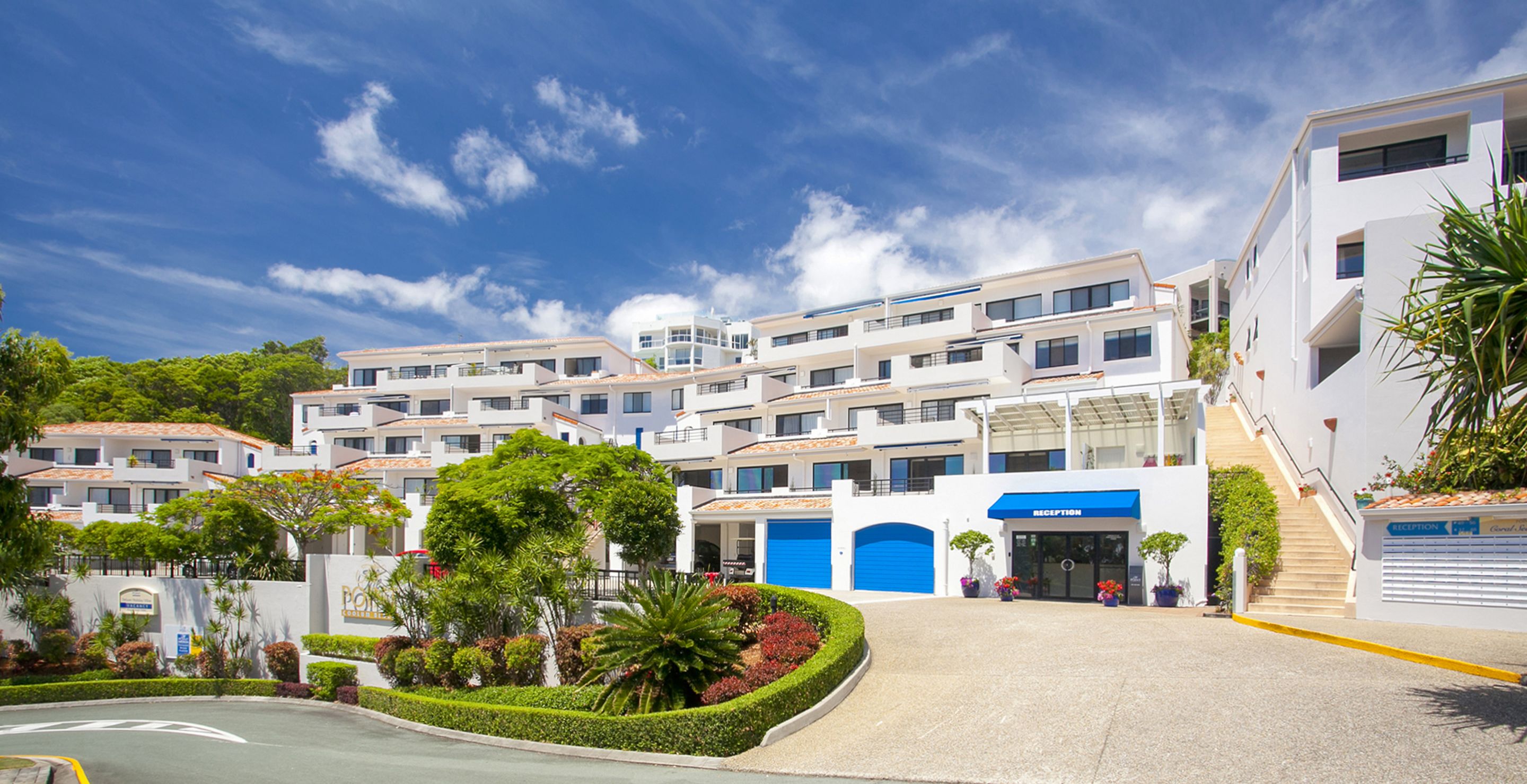 Un hotel moderno con varios pisos, una zona de recepción y un patio ajardinado con diversas plantas.