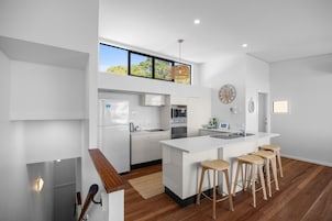A modern kitchen with a central island, bar stools, and a large window.