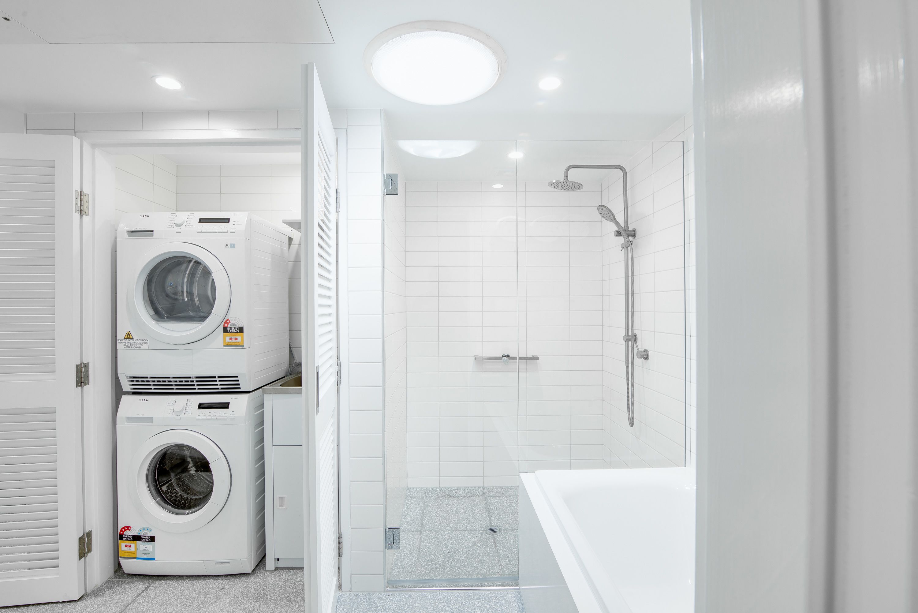Un baño moderno con lavadora y secadora integradas, ducha con cerramiento de vidrio y bañera blanca.