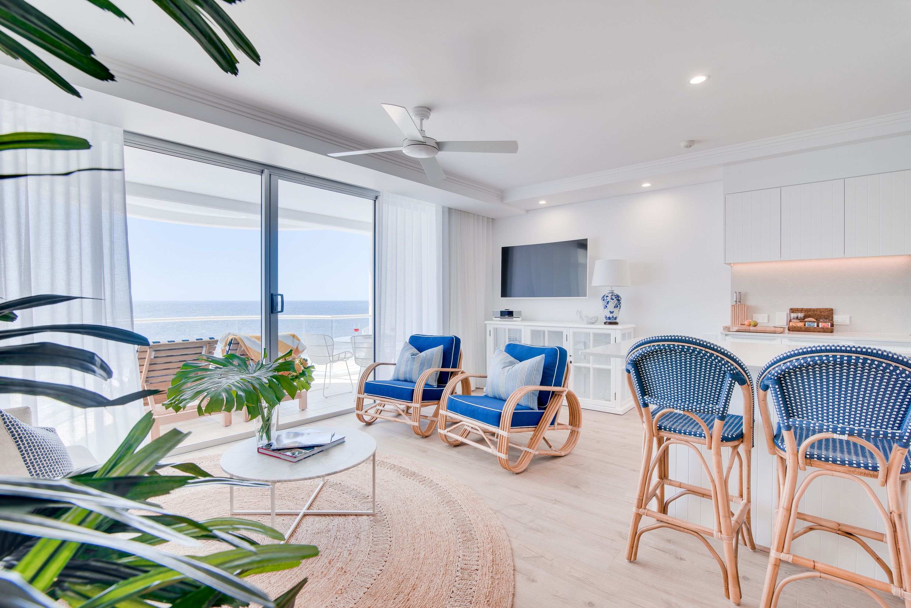 Ein modernes Wohnzimmer mit Rattanmöbeln, einem Flachbildfernseher und Blick auf den Ozean.