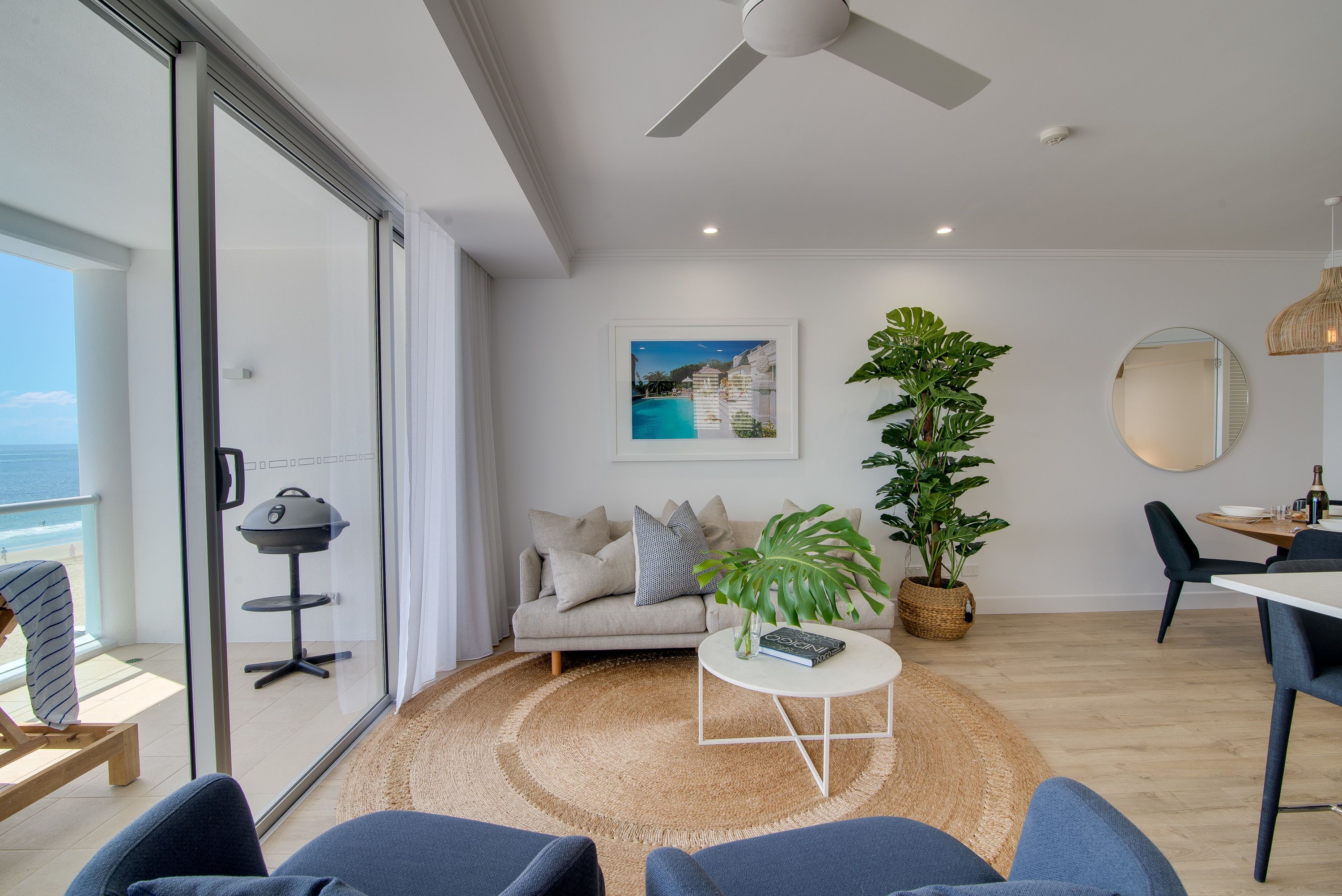 Uma sala de estar moderna com sofá, mesa de centro e vista para o oceano através de grandes portas de vidro.
