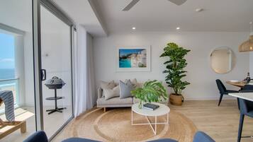 Uma sala de estar moderna com sofá, mesa de centro e vista para o oceano através de grandes portas de vidro.