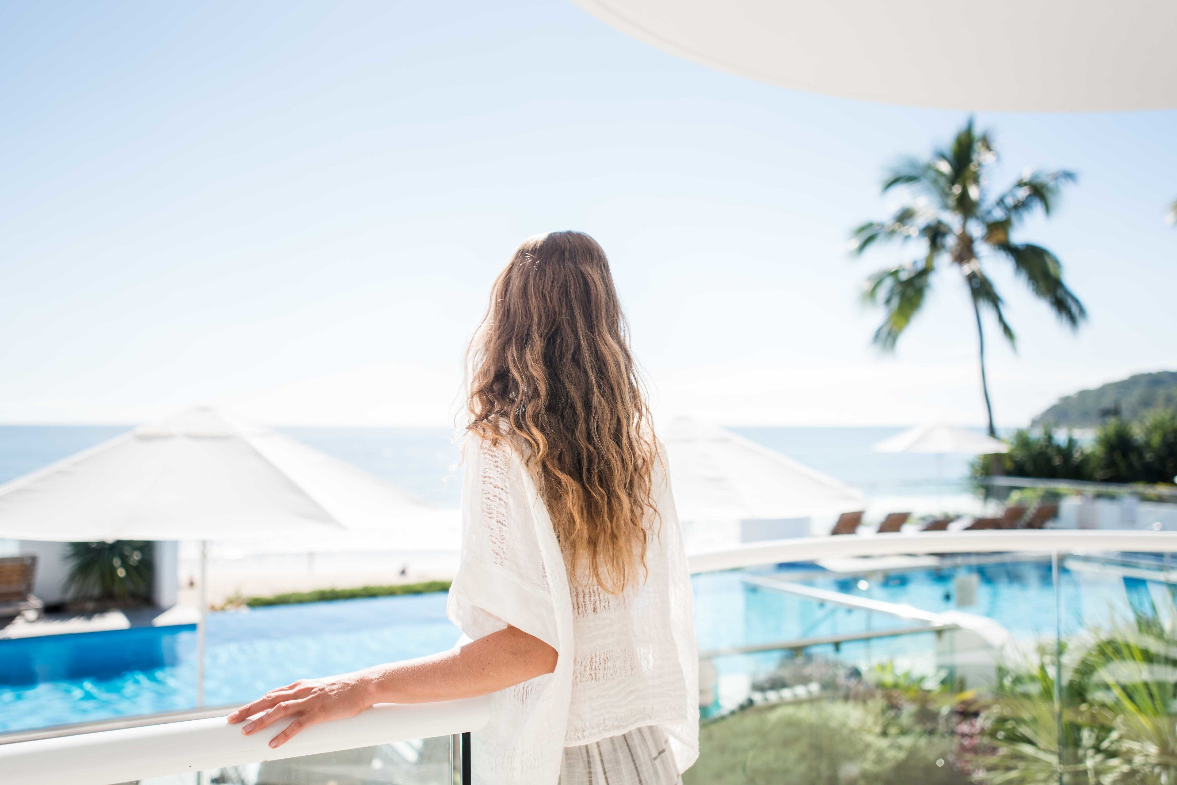 A person standing by a pool with a view of the ocean and palm trees.