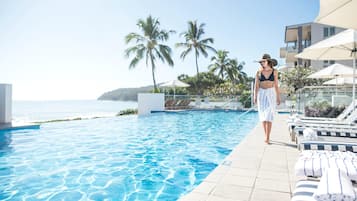 Una piscina al aire libre, sombrillas, sillones reclinables de piscina