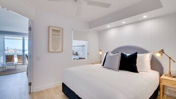 A bedroom with a large bed, a ceiling fan, a bedside lamp, and a view through a glass door to an outdoor area.
