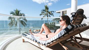 A person relaxing on a sun lounger with a view of the ocean and palm trees.