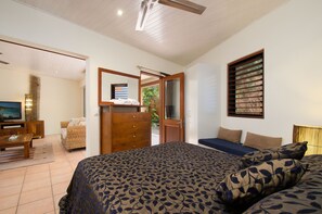 A bedroom with a bed, a television, a wooden dresser, a wicker chair, and a window with blinds.