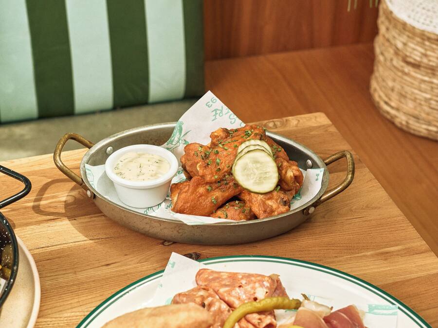 A dining table with a plate of fried chicken, a bowl of dipping sauce, and a plate of sliced meats.