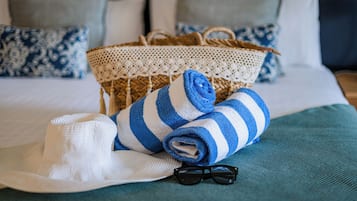 A neatly made bed with a blue and white striped towel, a white hat, and a pair of sunglasses on a teal bedspread.
