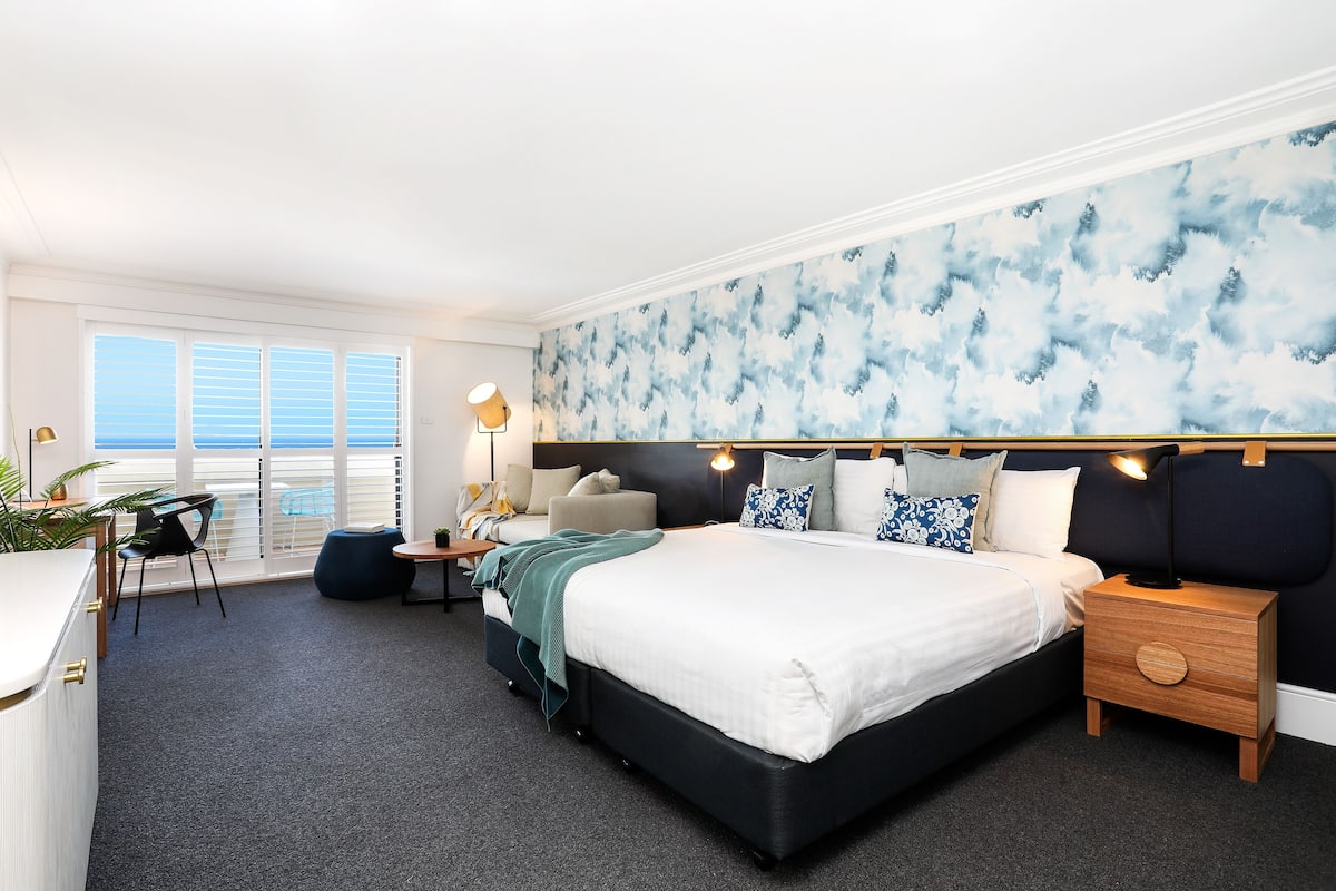 A modern bedroom with a large bed, bedside tables, a desk, and a chair.