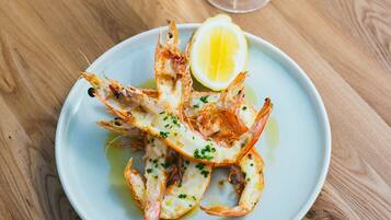 A plate of cooked shrimp with lemon and herbs, accompanied by a glass of white wine on a wooden table.