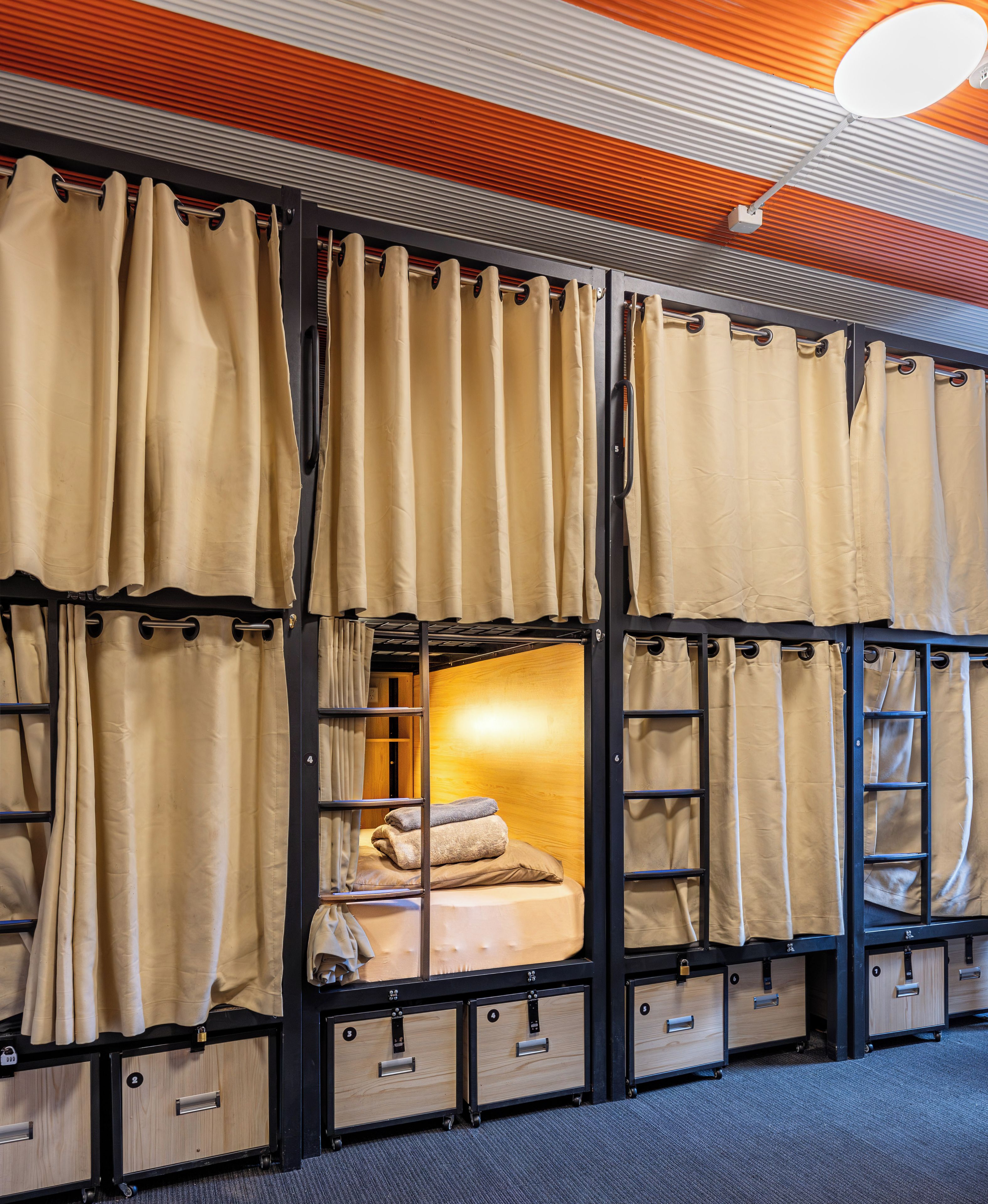 Habitación con literas, cortinas, una cama y cajones para guardar objetos.