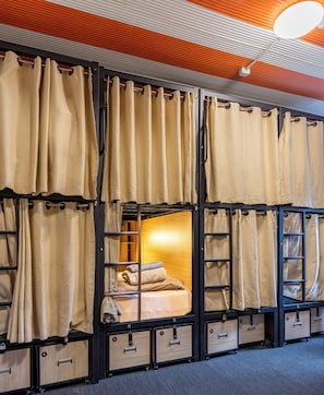 Habitación con literas, cortinas, una cama y cajones para guardar objetos.