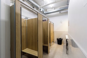 Des toilettes publiques avec des cabines en bois, une poubelle et un sèche-mains.