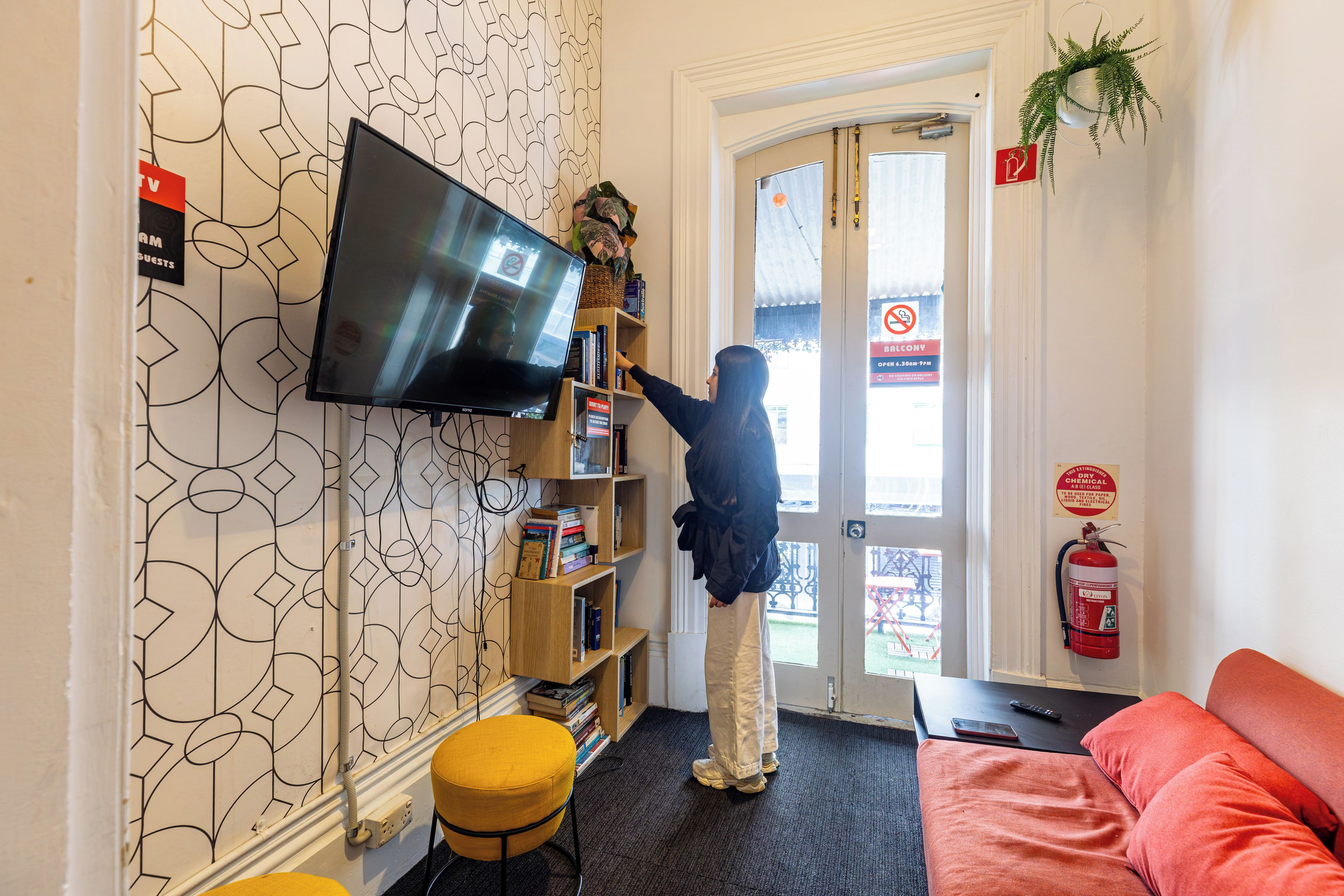 Habitación con una televisión montada en la pared, una estantería, un extintor y un sofá rojo.