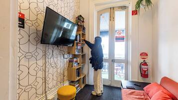 Habitación con una televisión montada en la pared, una estantería, un extintor y un sofá rojo.
