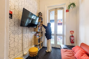 Habitación con una televisión montada en la pared, una estantería, un extintor y un sofá rojo.