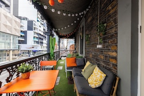 Un balcón con sofá, sillas y una mesa, con vistas a un paisaje urbano.