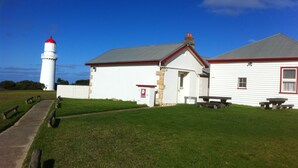 A lighthouse and a white building with a red roof, a picnic table, and a stone wall. - Cape Schanck Lighthouse (Boneo)