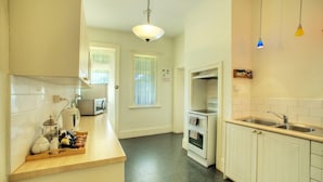 A kitchen with white cabinets, a microwave, a kettle, and a wooden tray with food. - Cape Schanck Lighthouse (Boneo)