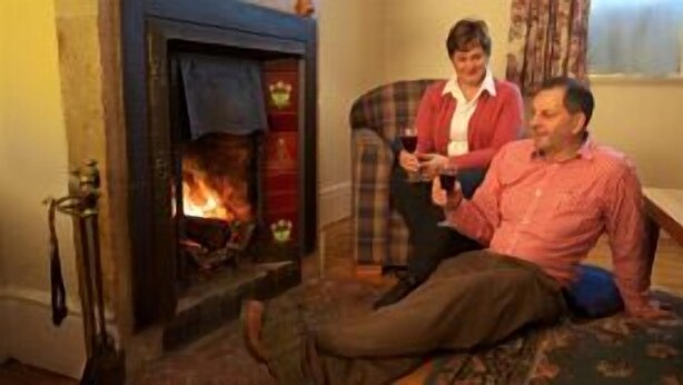 A room with a fireplace, a plaid armchair, and a person sitting on the floor holding a glass. - Cape Schanck Lighthouse (Boneo)