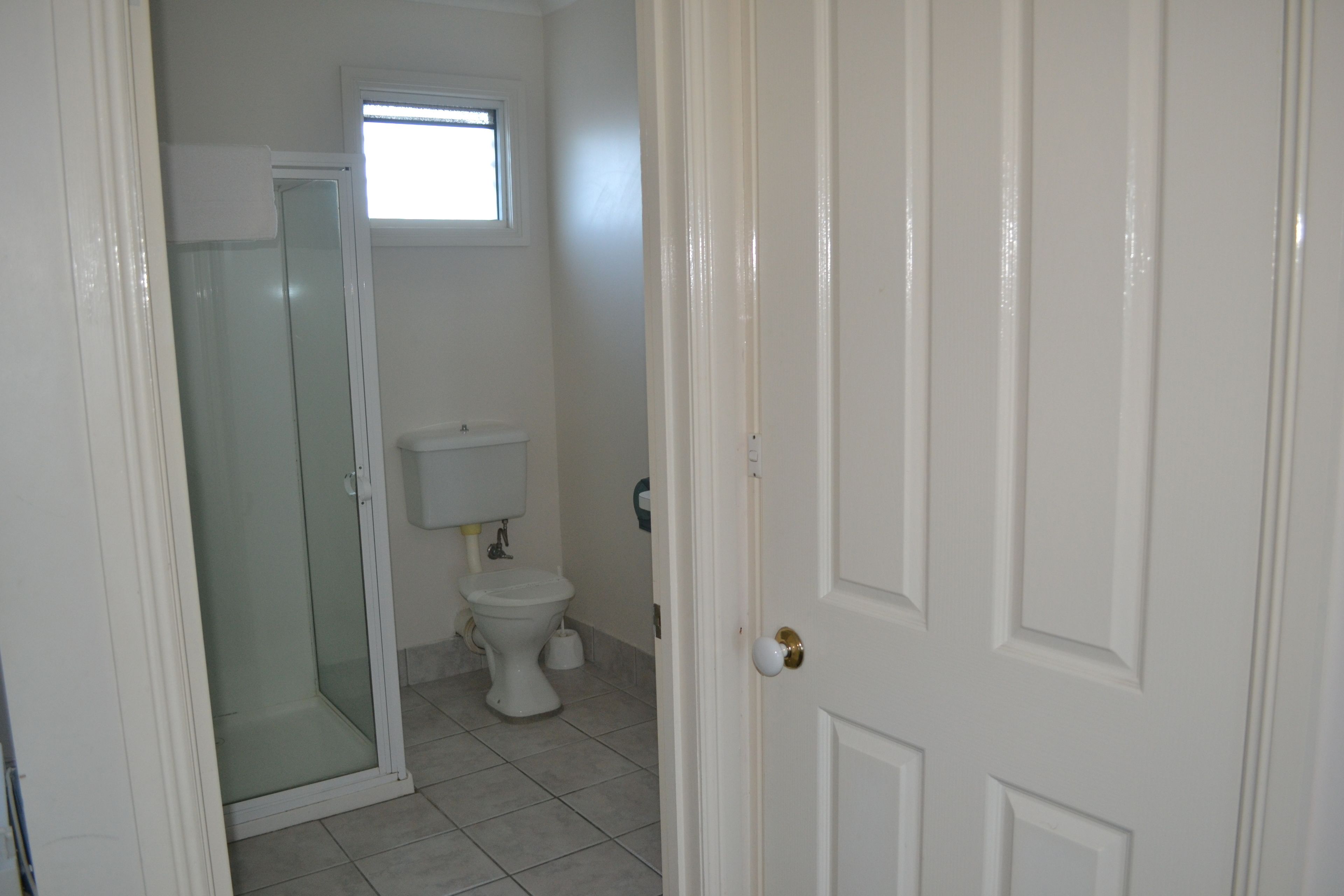 A bathroom with a glass shower enclosure, a toilet, and a window above the toilet.