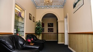 A hallway with black leather chairs, a potted plant, framed artwork on the walls, and a chandelier. - Hobart Tower Motel (New Town)