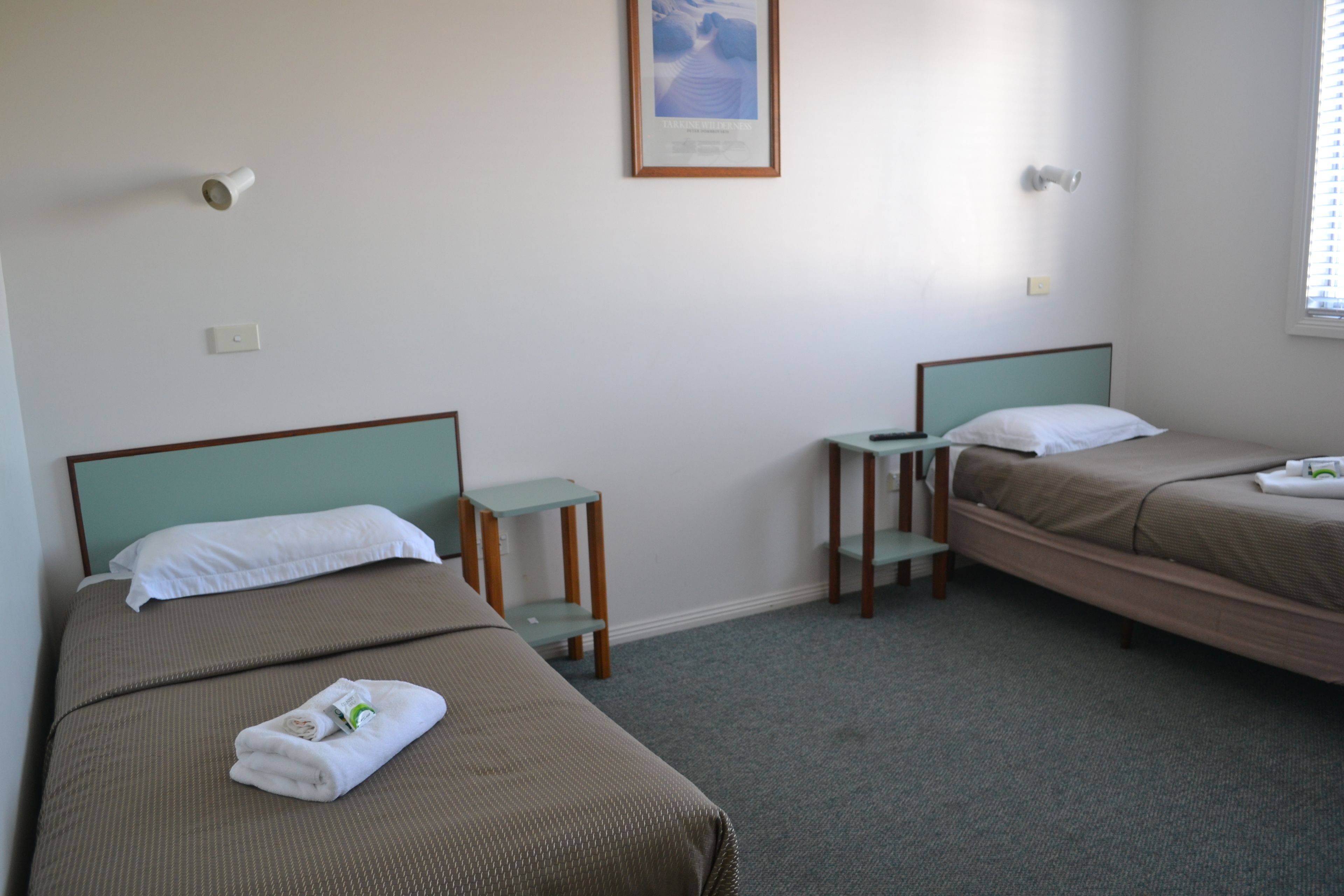 A hotel room with two single beds, a small table, and a framed picture on the wall.